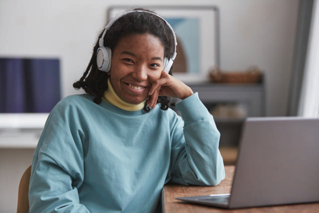 En student med headphones som sitter med en PC og smiler til kamera